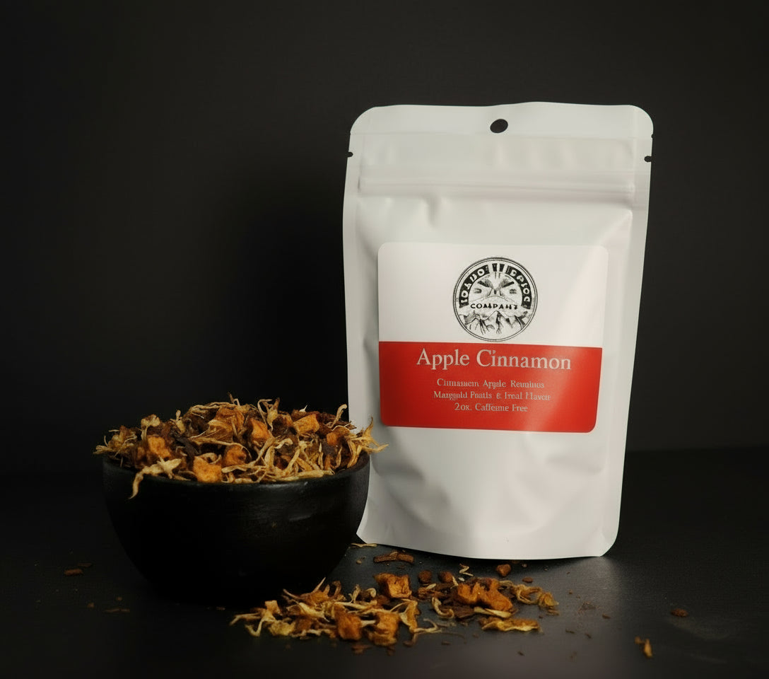 White packaging of Apple Cinnamon tea with a black bowl of dried herbs on a dark background