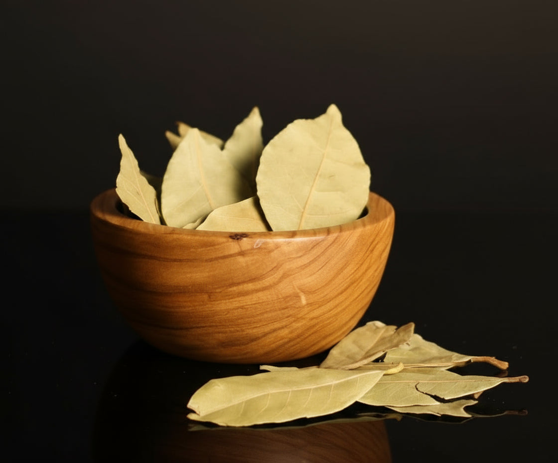 Wooden bowl filled with dried bay leaves on a dark surface.