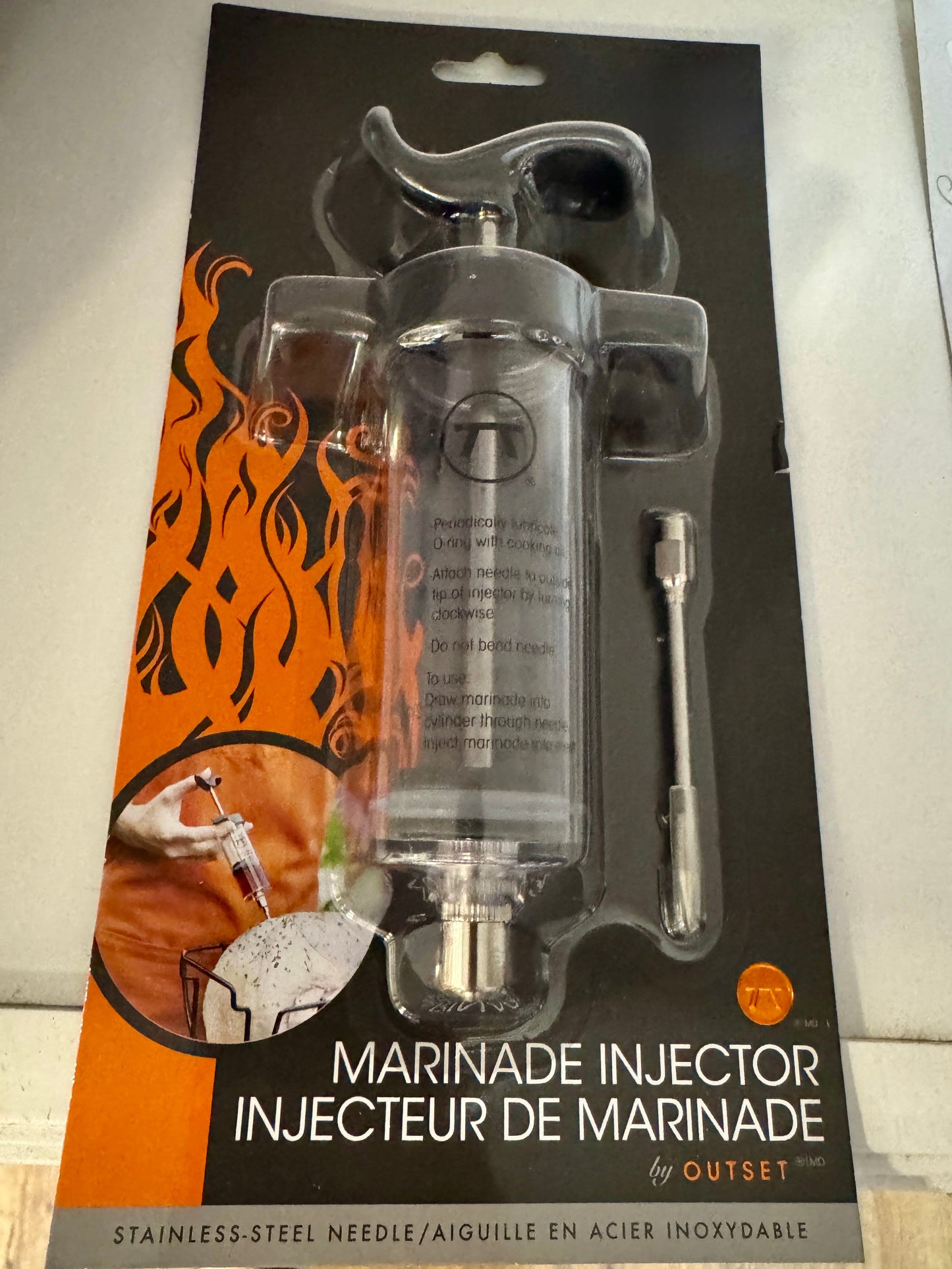 Marinade injector with packaging featuring flames and branding on a white background