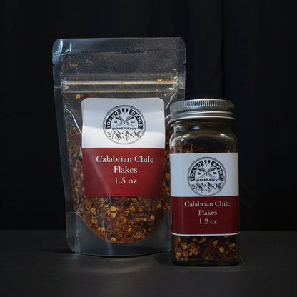 Two spice containers labeled 'Calabrian Chile Flakes' on a dark background