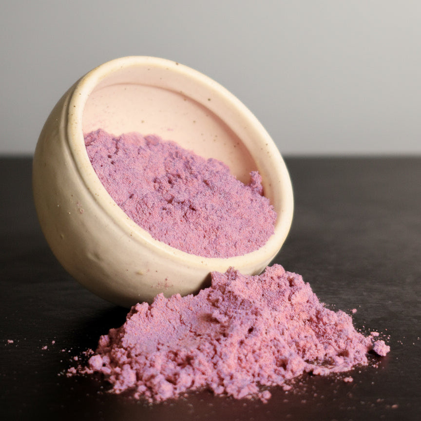 Acai powder spilling out of a beige bowl on a dark surface with a gray background