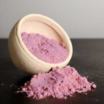 Acai powder spilling out of a beige bowl on a dark surface with a gray background