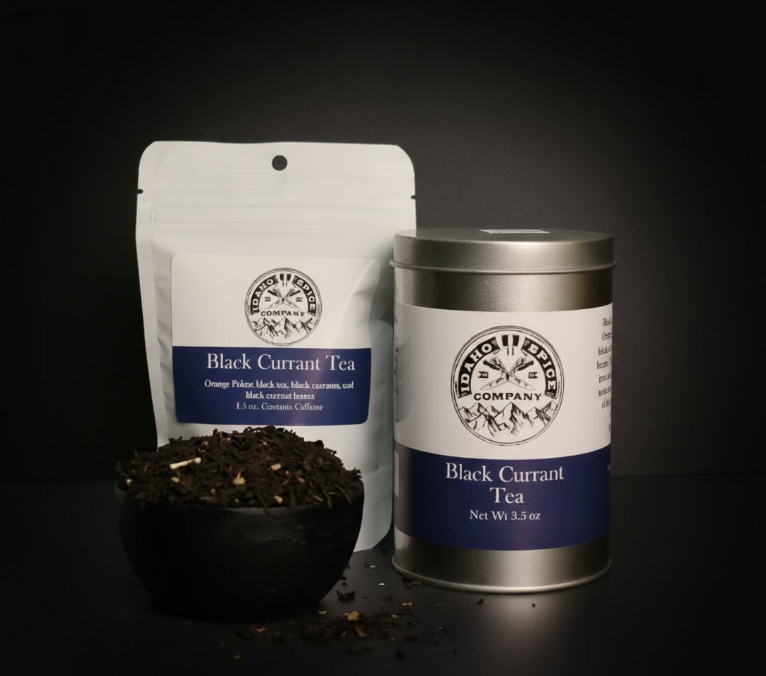 Black Currant Tea packaging including a bag, canister, and bowl of tea leaves on a dark background.