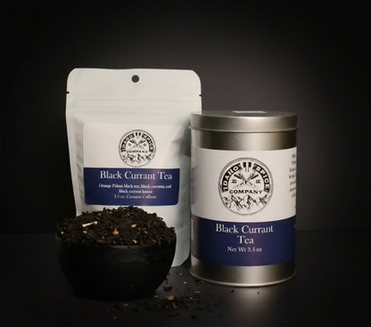 Black Currant Tea packaging including a bag, canister, and bowl of tea leaves on a dark background.
