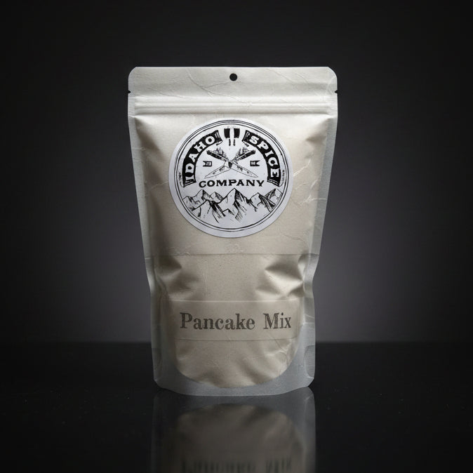 Pouch of Idaho Spice Company pancake mix on a reflective black surface with a dark background