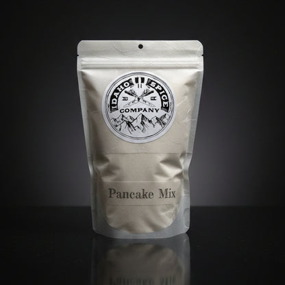 Pouch of Idaho Spice Company pancake mix on a reflective black surface with a dark background